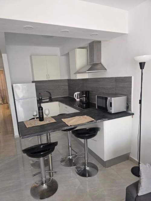 Moderna cocina con muebles blancos, encimera oscura, barra americana y electrodomésticos de acero inoxidable en Smart Rent Fuerteventura