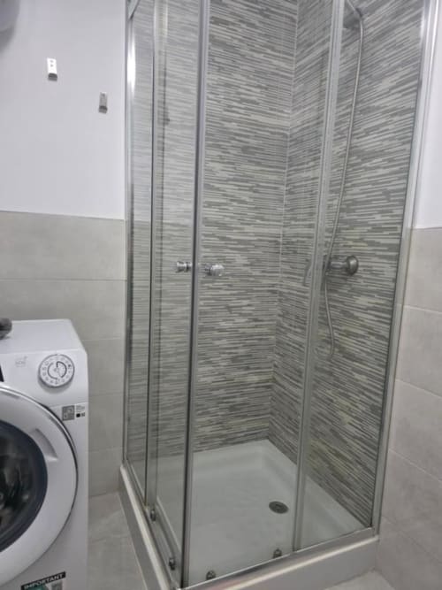 Moderno cubículo de ducha con azulejos grises y puertas de cristal en apartamento Smart Rent Fuerteventura