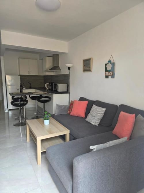Moderno estudio con cocina abierta, barra negra, sofá gris con cojines coral y mesa de madera en Smart