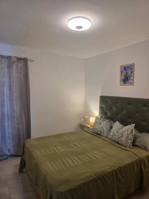 Dormitorio moderno en apartamento Sonia Beach Stay, Fuerteventura, con cama de cabecera verde y luminaria de techo