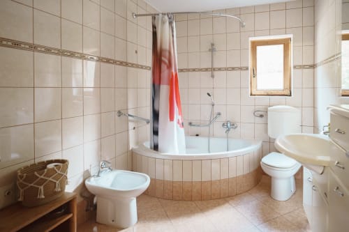 Spacious bathroom in Pine Suite at Kmetija Pečnik with curved corner bathtub, dual sinks, and cream-colored tiles