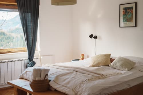 Bright mountain-view bedroom at Kmetija Pečnik with cream bedding, wooden flooring, and alpine landscape visible through