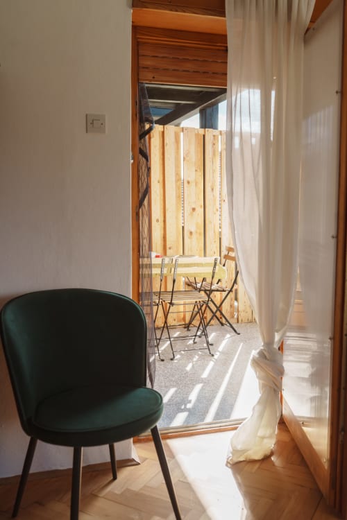 Green chair facing open door to Borovc Suite balcony with wooden deck and seating at Kmetija Pečnik, Prevalje
