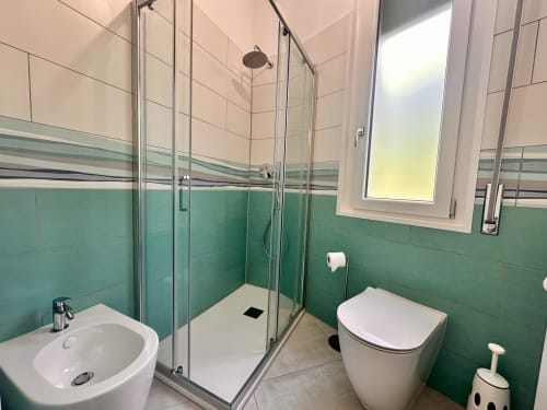 Bagno moderno con piastrelle verdi, cabina doccia, lavabo e toilette presso l'appartamento Antico Mulino, Varigotti