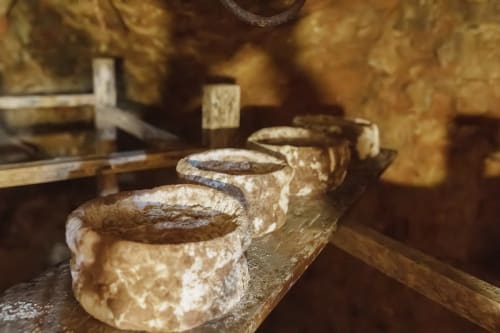 Rustic wooden wine racks with aged cheese wheels at Kmetija Pečnik farmhouse in Prevalje