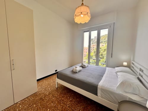 Camera luminosa nell'appartamento di Varigotti con balcone vista mare, letto bianco, pavimentazione in sughero e lampada a sospensione