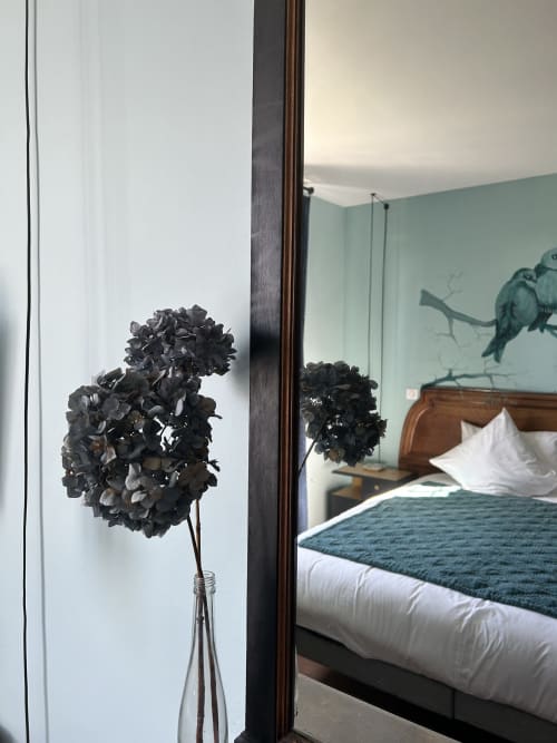 Dried black hydrangea in glass vase beside mirror reflecting bedroom at Le Clos d'Azel, Alsace
