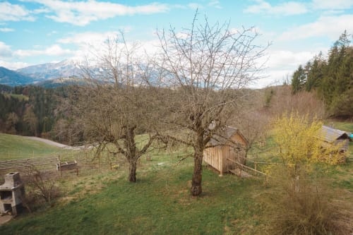 Rural farmhouse garden at Kmetija Pečnik with bare fruit trees, mountain view, wooden structures, and Alpine landscape in