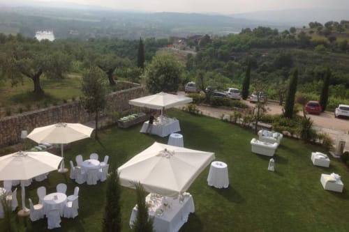 Elegante allestimento matrimoniale all'aperto presso la venue di Verona con ombrelloni bianchi, tavoli rotondi e cipressi che si affacciano sulla Toscana