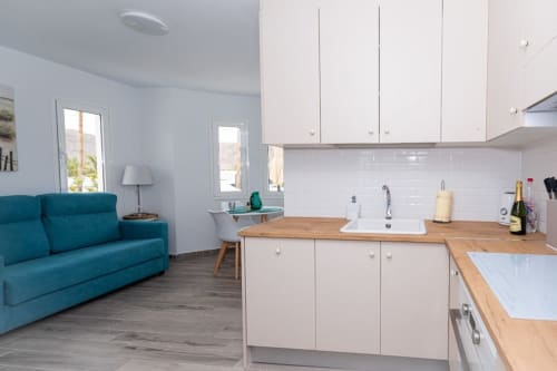 Cocina y sala de estar de planta abierta en apartamento Casa Andre con muebles blancos, encimeras de madera, sofá turquesa y ventanas