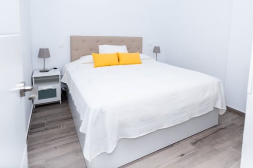 Dormitorio moderno en Casa Andre, Smart Rent Fuerteventura, con cabecero beige, ropa de cama blanca y almohadas decorativas amarillas