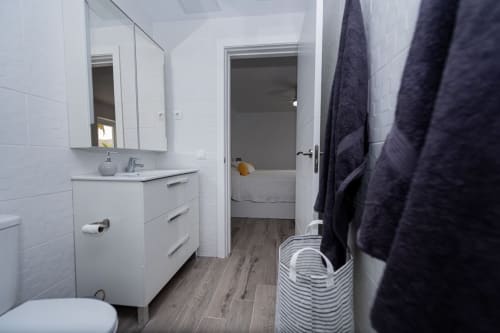 Baño moderno en apartamento Casa Andre, Smart Rent Fuerteventura con azulejos blancos, tocador, espejo y toallas oscuras