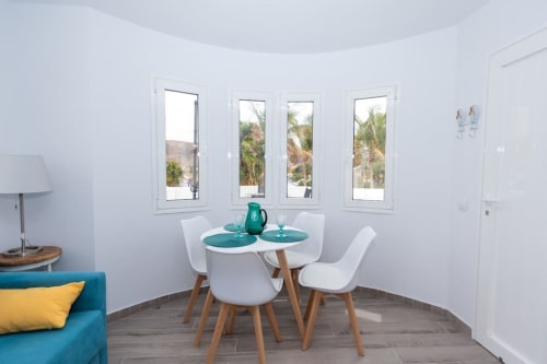 Zona de comedor moderna en apartamento Casa Andre con mesa redonda blanca e iluminación natural desde ventanales con vistas a Fuerteventura