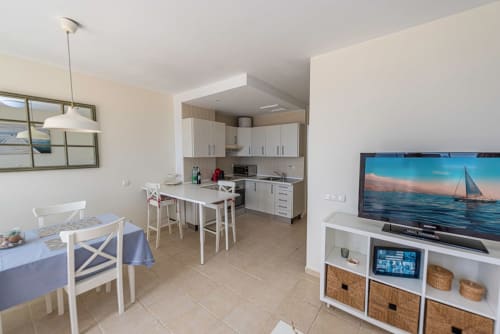 Cocina abierta y sala de estar modernas con muebles blancos, mesa de comedor, TV y decoración con temática de playa en Smart