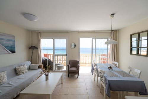 Luminoso apartamento frente al mar en Fuerteventura con vistas océano, mobiliario moderno, comedor y acceso a balcón
