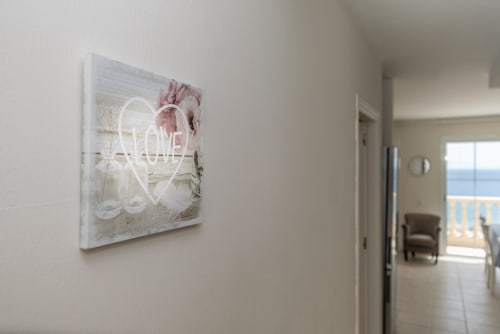 Cartel neón 'LOVE' sobre lienzo blanco en pasillo moderno con vistas al océano, Smart Rent Fuerteventura