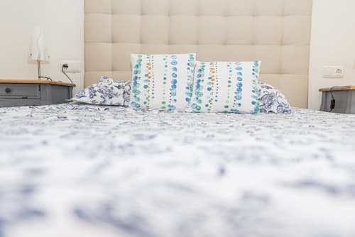 Dormitorio moderno en Smart Rent Fuerteventura con cabecero acolchado beige, almohadas azules estampadas y ropa de cama blanca en Bernardo