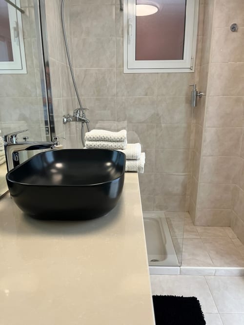 Baño moderno en Smart Rent Fuerteventura con lavamanos tipo vessel negro, ducha de lluvia y azulejos en tonos beige