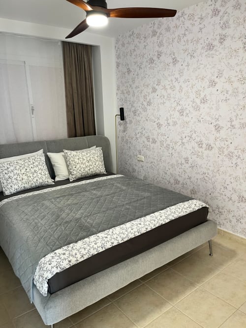 Moderno dormitorio en Smart Rent Fuerteventura con cama matrimonial, papel tapiz floral, ventilador de techo y baldosas beige