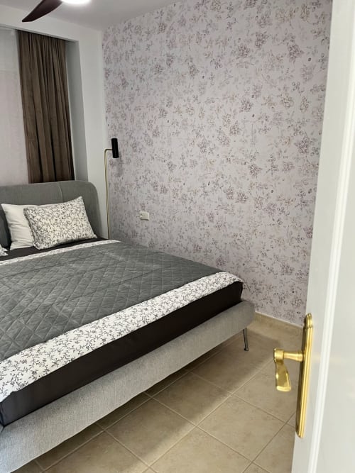 Dormitorio moderno en apartamento Smart Rent Fuerteventura con cama gris, papel tapiz floral y piso de baldosas