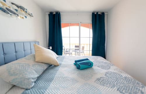 Dormitorio luminoso en Casa Sky con cabecera de cama azul, ropa de cama estampada y balcón con vistas al océano en Fuerteventura