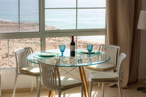 Área de comedor moderno en Casa Sky con vistas al océano y playa, grandes ventanales, mesa de cristal, sillas blancas y botella de vino