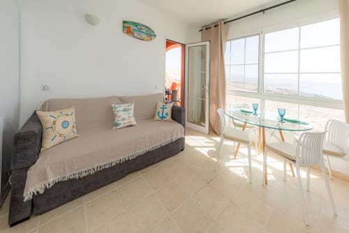 Luminoso apartamento Casa Sky en Fuerteventura con vistas al océano, sofá beige, mesa de comedor de cristal y decoración temática de playa