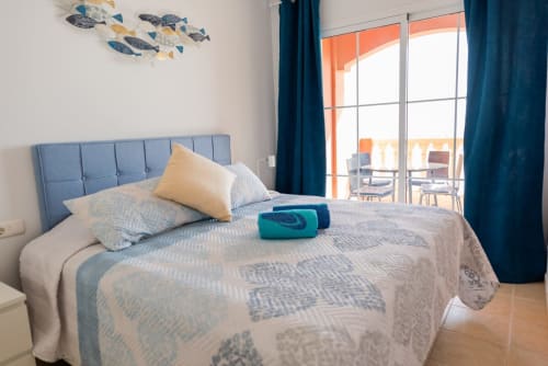 Dormitorio moderno en Smart Rent Fuerteventura con cabecero azul, ropa de cama estampada y balcón con vista al océano en Casa Sky