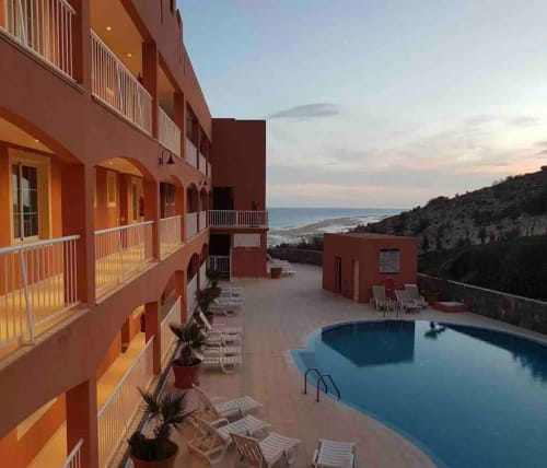 Complejo de apartamentos de terracota con piscina con vistas a la costa de Fuerteventura al atardecer, barandillas blancas y palmeras visibles