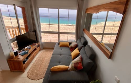 Moderno apartamento frente al mar en Fuerteventura con vistas al océano, sofá gris, muebles de madera y playa arenosa