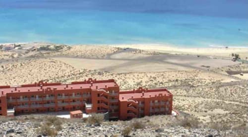 Edificios de apartamentos rojo en paisaje desértico, resort Smart Rent Fuerteventura con vistas al océano