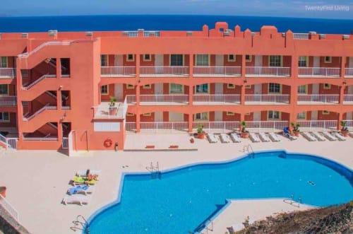 Resort de playa con arquitectura coral brillante, piscina azul curva, tumbonas y vistas al océano en Fuerteventura