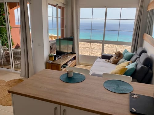 Moderno apartamento frente al mar en Fuerteventura con vistas al océano, zona de estar amueblada y dormitorio con vista a la playa