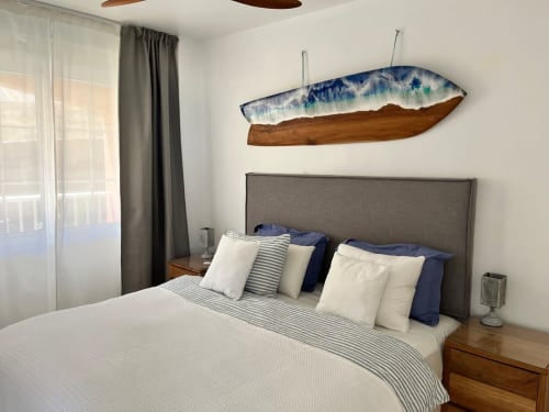 Recámara moderna con cabecera tapizada en gris, ropa de cama a rayas y arte en madera flotante en apartamento Casa Kiteloop