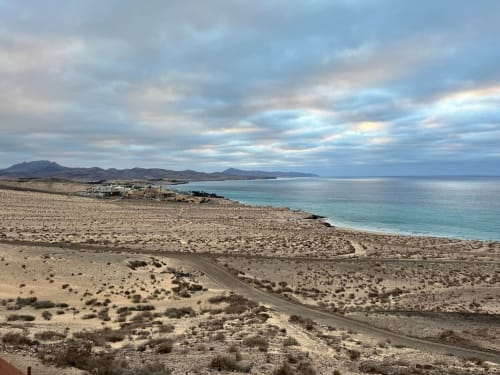 Paisaje costero frente al mar en Smart Rent Fuerteventura con aguas turquesas, terreno desértico arenoso y vistas de montaña