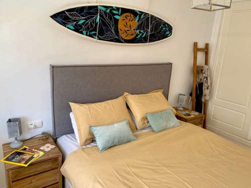 Habitación moderna con cabecera tapizada gris, ropa de cama amarilla, almohadas turquesas y arte decorativo de tabla de surf en Casa