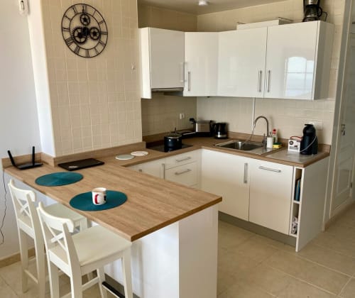 Cocina moderna con gabinetes blancos, encimeras de madera, barra para desayunar y electrodomésticos de acero inoxidable en Casa