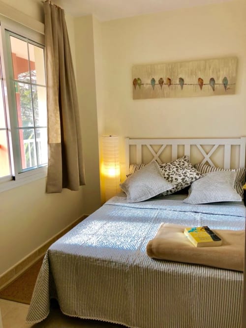 Dormitorio luminoso en apartamento Elisabeth de Smart Rent Fuerteventura con ropa de cama a rayas, cabecero geométrico y vista al océano