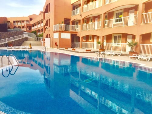 Complejo residencial Smart Rent Fuerteventura con piscina azul, edificios de terracota y barandillas blancas con vistas