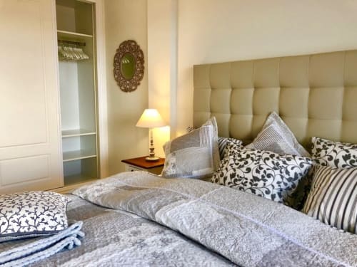 Dormitorio elegantemente amueblado en Smart Rent Fuerteventura con cabecero tapizado en beige, almohadas estampadas y lámpara de mesita
