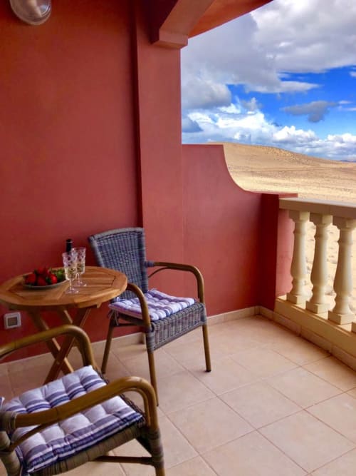 Terraza roja con sillas de mimbre, mesa de madera y vistas panorámicas al desierto en el apartamento Elisabeth de Smart Rent Fuerteventura