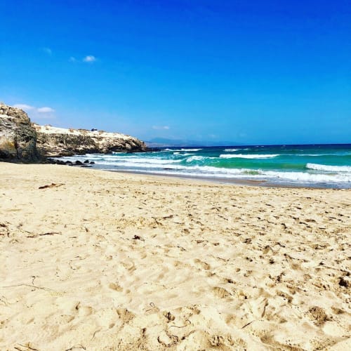 Playa de arena con olas turquesas y acantilados rocosos en Smart Rent Fuerteventura, apartamento frente al mar en España