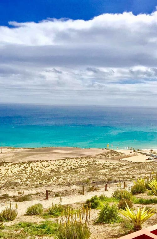 Playa turquesa y paisaje desértico en Smart Rent Fuerteventura con arena blanca y cielo azul