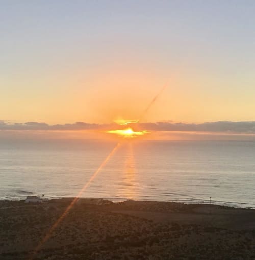 Amanecer dorado sobre el océano desde la playa de Fuerteventura, reflejando luz dorada en aguas tranquilas con montañas distantes