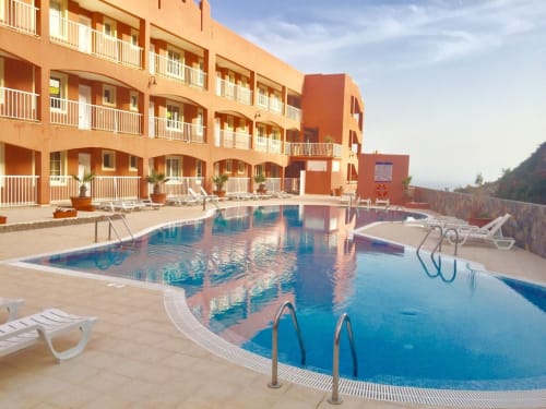 Resort de playa Smart Rent Fuerteventura con balcones curvos naranjas frente a dos piscinas y vistas a las montañas