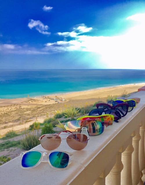 Gafas de sol coloridas alineadas en el balcón de la playa con vistas al agua turquesa y arena blanca en el resort de Fuerteventura