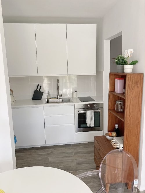 Cocina moderna blanca en apartamento Fuerte Hygge de Smart Rent Fuerteventura con horno de acero inoxidable, fregadero y estanterías de madera