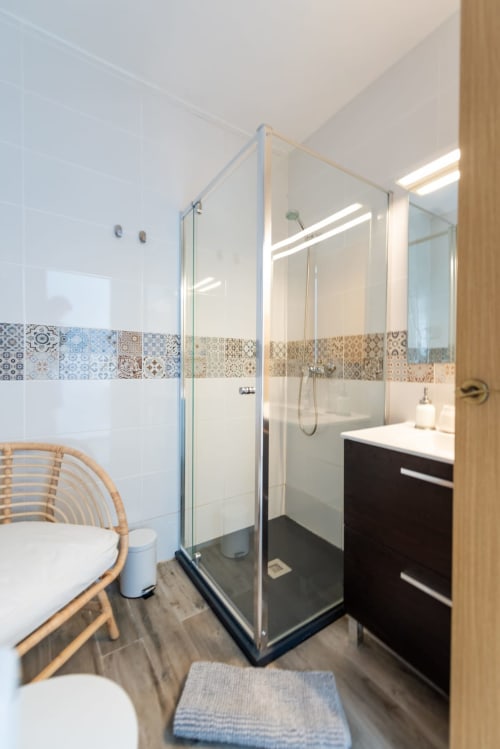 Baño moderno en apartamento Fuerte Hygge de Smart Rent Fuerteventura con ducha de cristal, tocador negro, inodoro y detalles decorativos