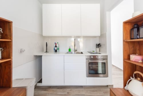 Cocina moderna blanca con horno de acero inoxidable, estantería de madera y fregadero en apartamento Fuerte Hygge de Smart Rent