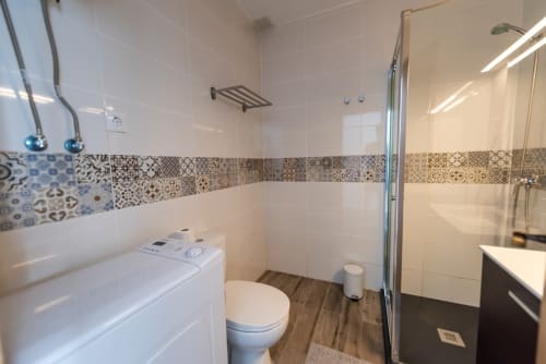 Baño moderno en apartamento Fuerte Hygge con azulejos blancos, cenefa decorativa, ducha tipo walk-in, inodoro y tocador